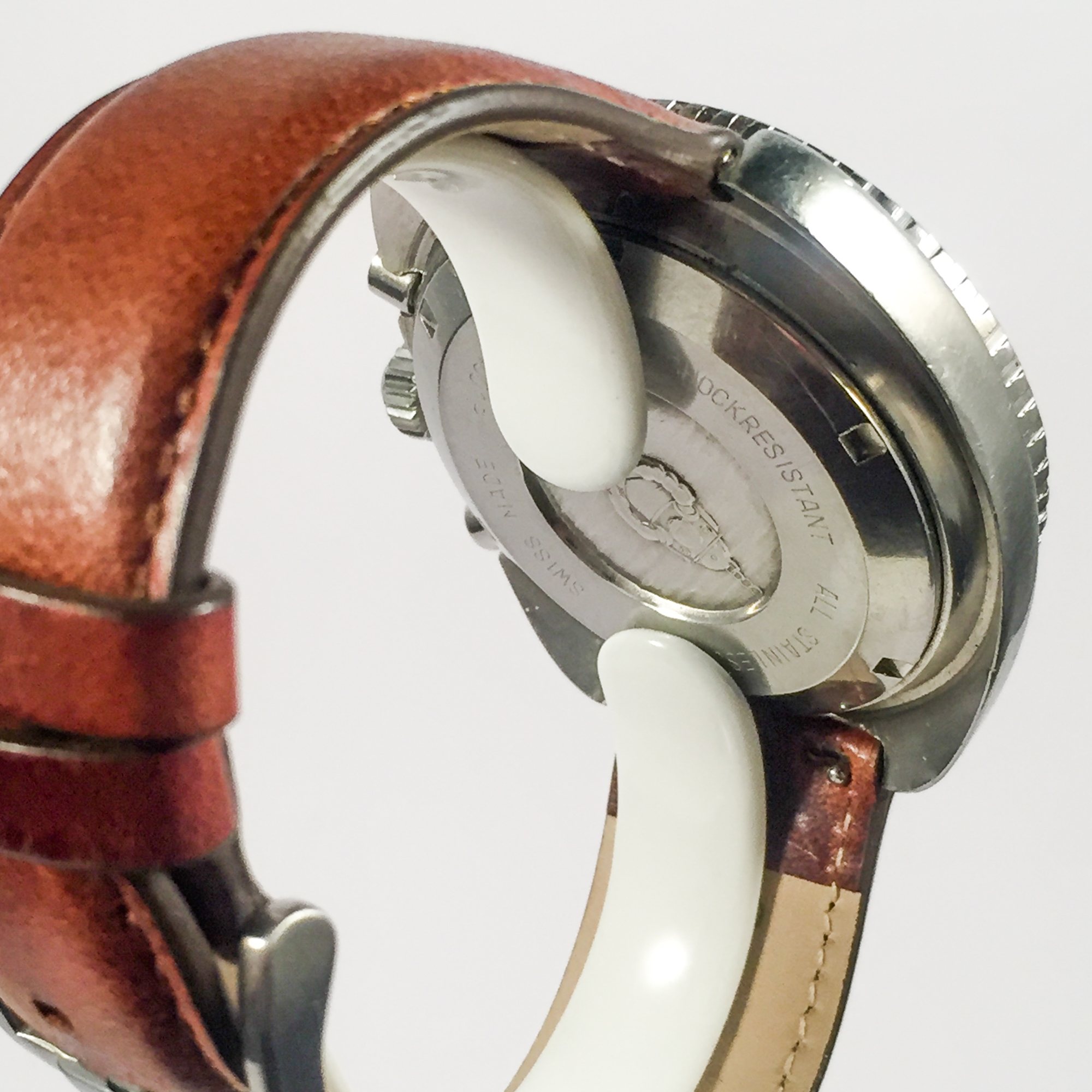 Vue du fond de boîtier gravé d'une montre en acier inoxydable avec bracelet en cuir brun, posée sur un support blanc devant un fond uni.